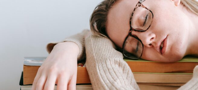 Begleitsätze, die ihr vermeiden solltet: Eine junge Frau schläft auf einem Stapel Bücher, vermutlich nachdem sie zu viele davon gelesen hat