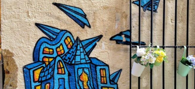 Streetart in Montpellier: Ein Haus steht auf einem aufgeschlagenen Buch. Um es herum schwirren Papierflieger.